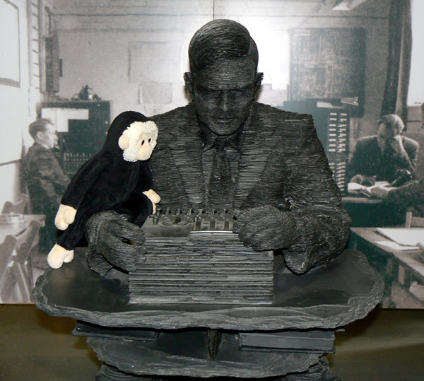 Mooch monkey sits on the statue of Alan Turing working an Enigma.